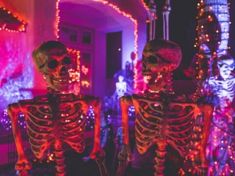 two skeleton near white concrete building with string lights at daytime