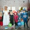 children standing while holding Jack 'o lantern and wearing costume