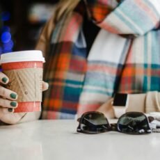 woman holding white disposable cup while leaning on table